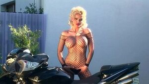 Busty blonde teases on a motorcycle in fishnet